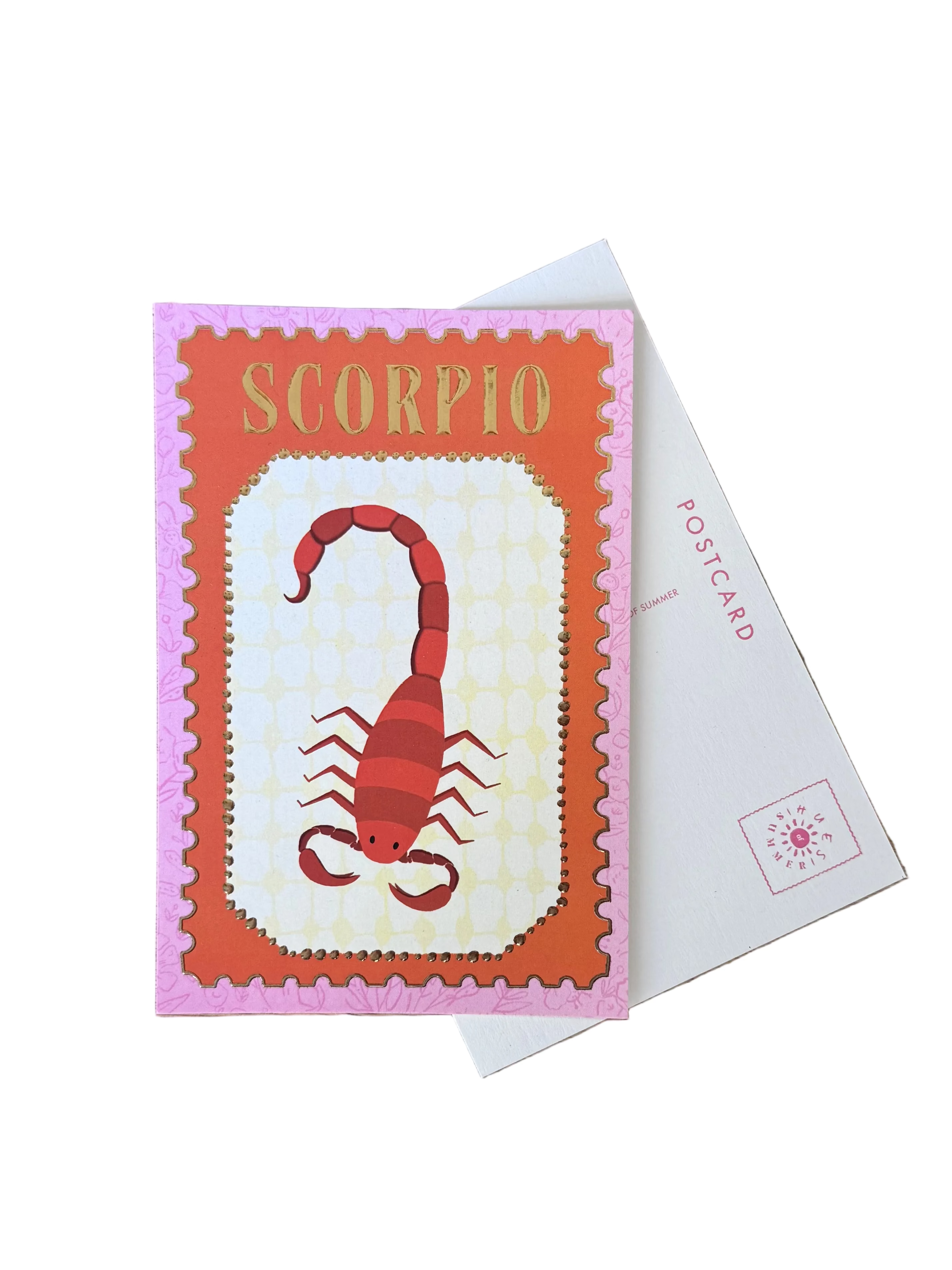 A Scorpion-themed postcard with a red scorpion illustration on an orange and pink background, displayed on a wooden table next to other colorful postcards.