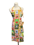 A multicolor apron with a vintage fruit-and-vegetable patchwork print is displayed on a white mannequin dress form. The apron features a yellow border and includes a front pocket holding two wooden spoons, set against a blue paneled wall background.