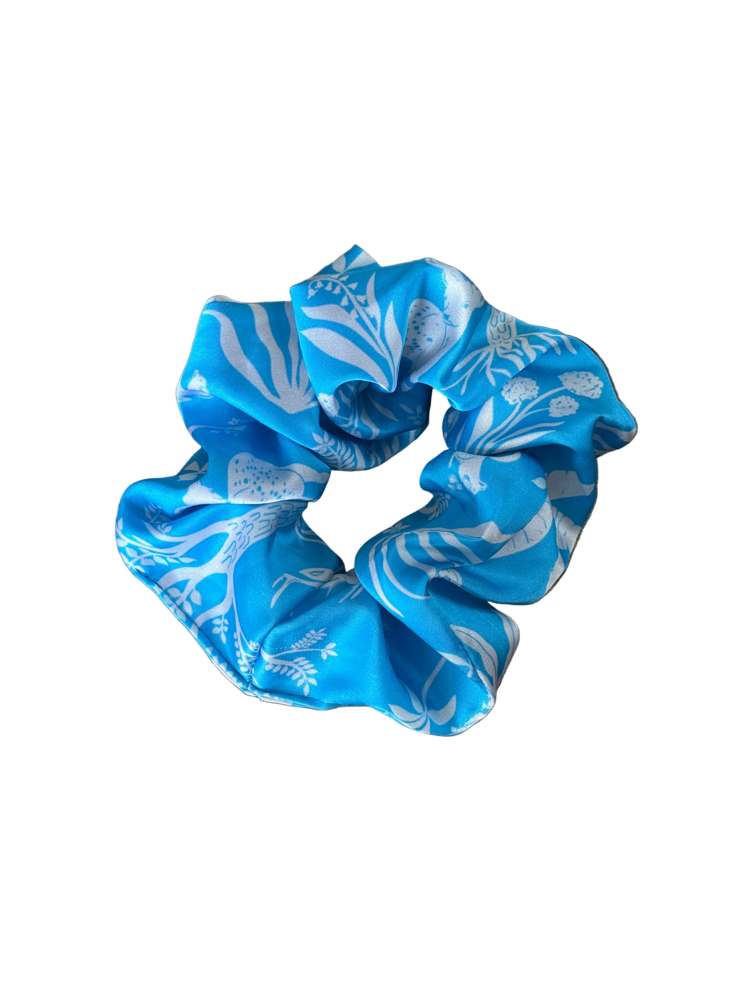 A blue fabric scrunchie with a white botanical pattern, resting on a wooden surface.