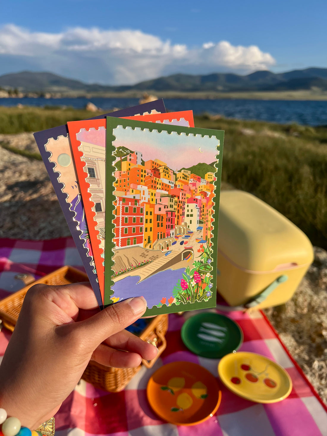 Hand holding a fan of postcards including Sunset in Cinque Terre, lake and mountains in background