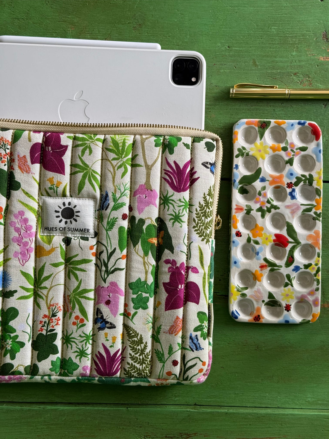 Ivory Bugs and Bloom quilted tablet sleeve holding a tablet, beside a matching cosmetic pouch