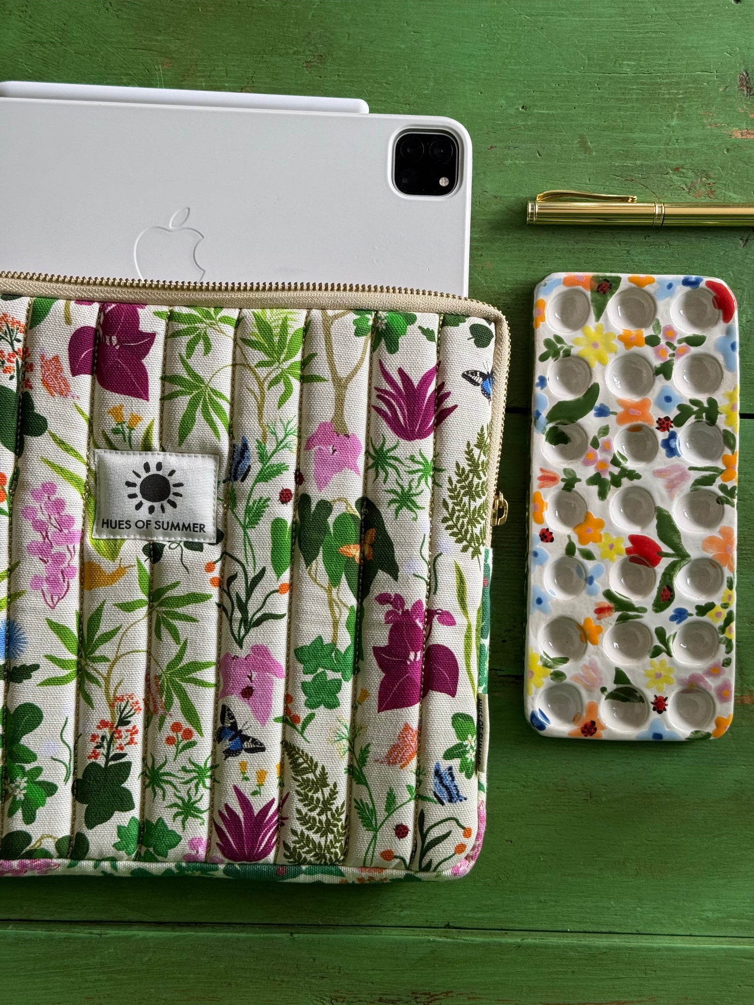 Ivory Bugs and Bloom quilted tablet sleeve holding a tablet, beside a matching cosmetic pouch